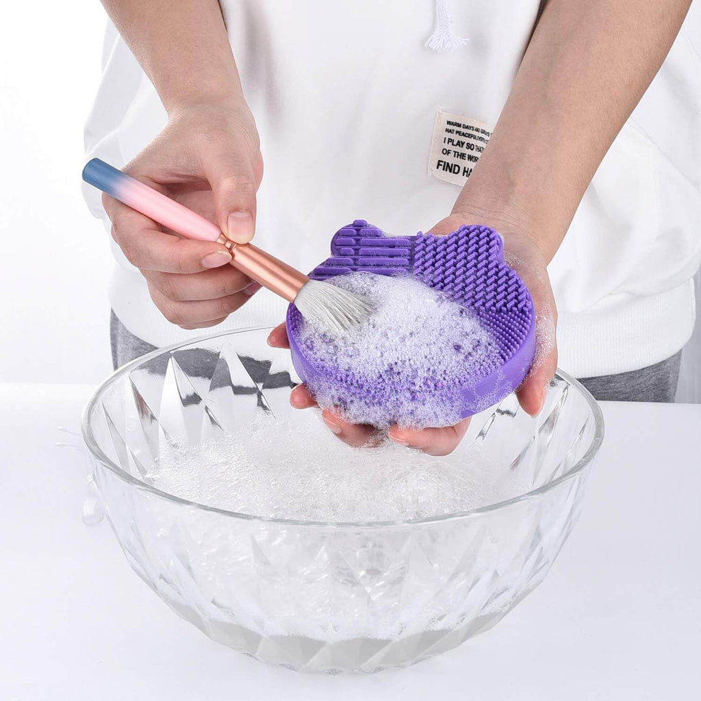 CleanMat – Siliconen Make-upborstelreiniger in gebruik met borstel en zeep in een kom.